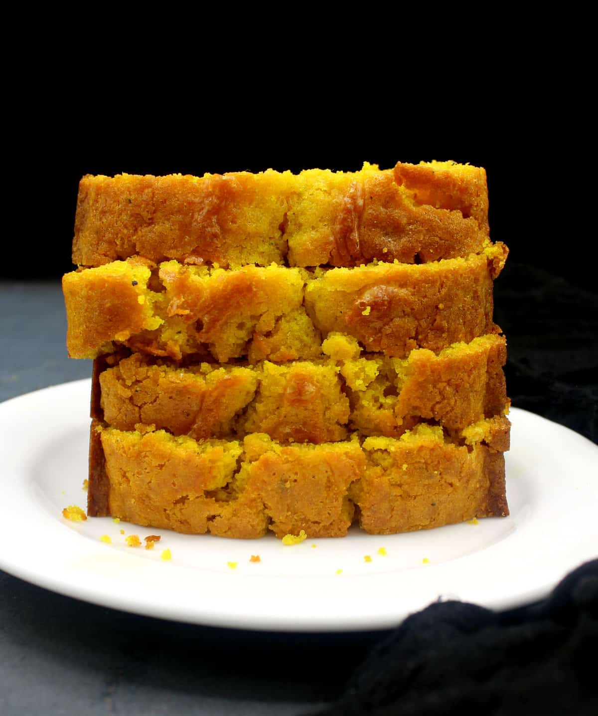 Four slices of vegan turmeric cake stacked on top of one another in a white dish.