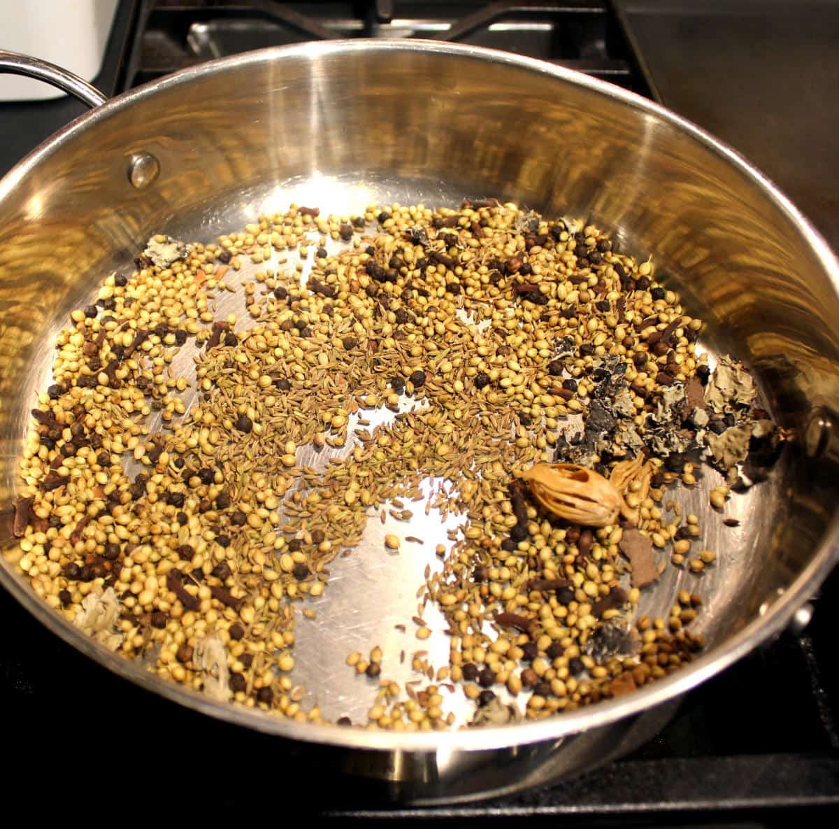 Fennel seeds, mace, coriander seeds, cumin seeds, stone flower and peppercorns roasting in a skillet.