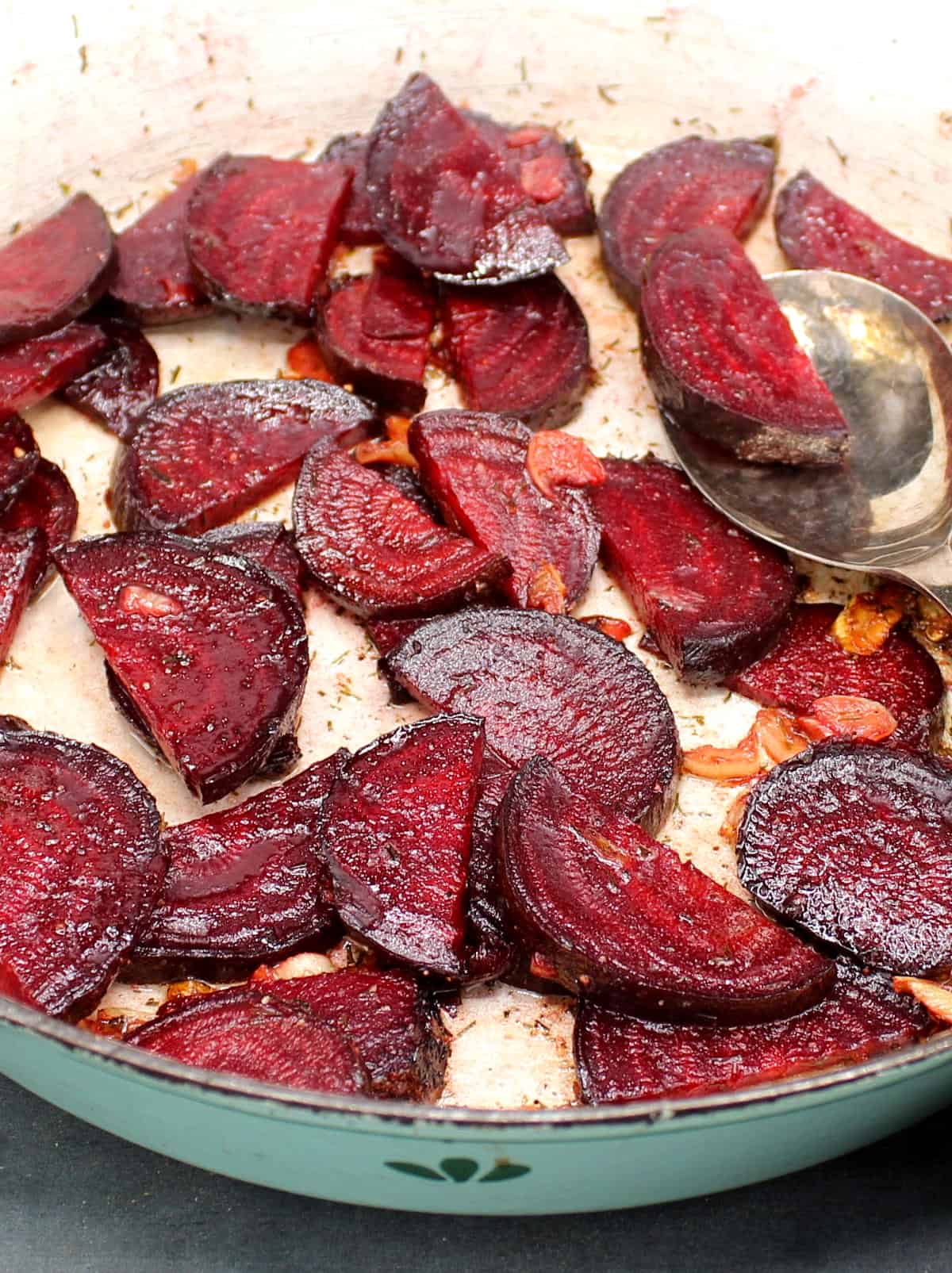 Close up of slices of deep red beetroot tossed with garlic and butter in a skillet.