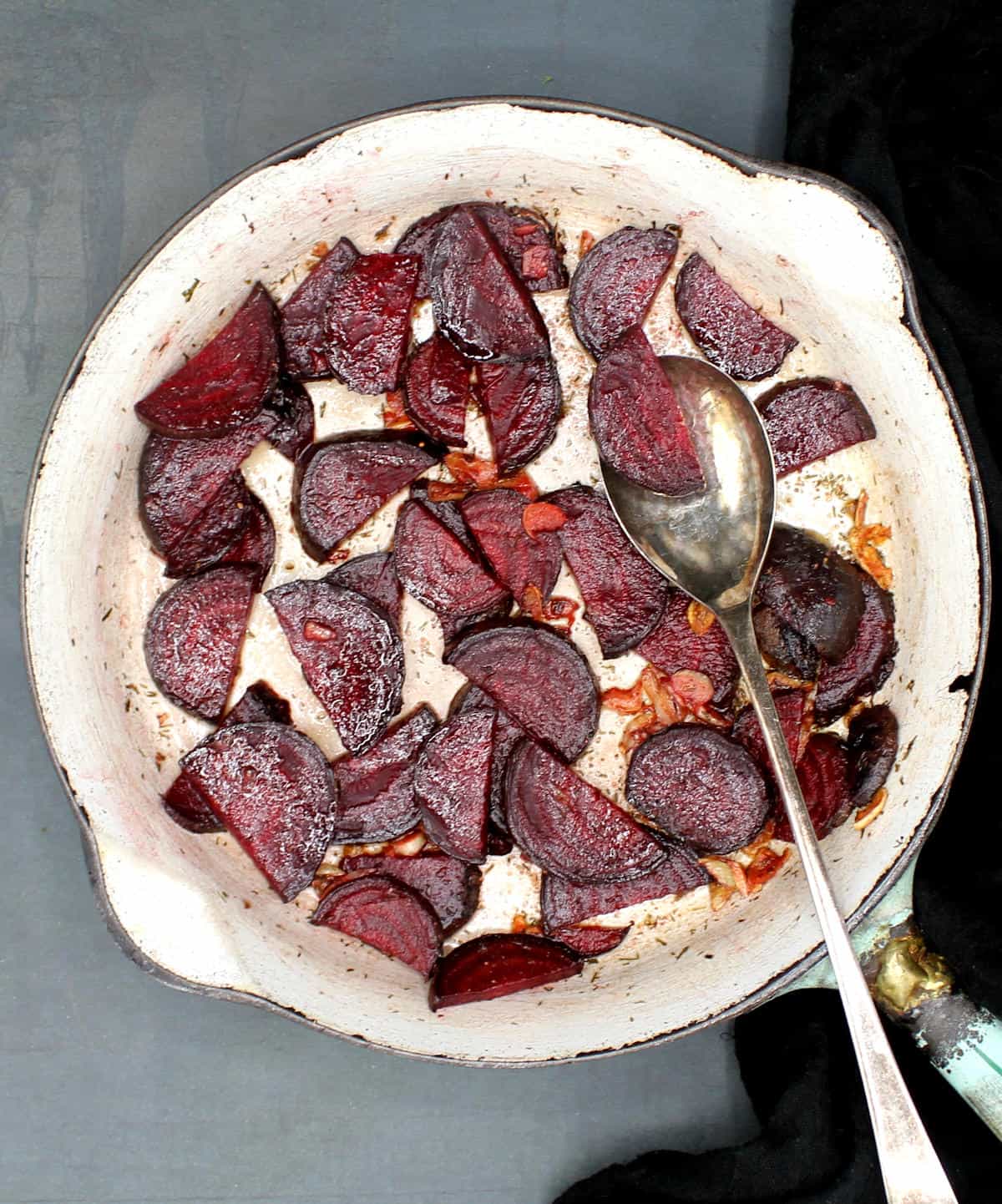 Overhead shot of a skillet with slices of deep red beetroot tossed with garlic and butter and a spoon.