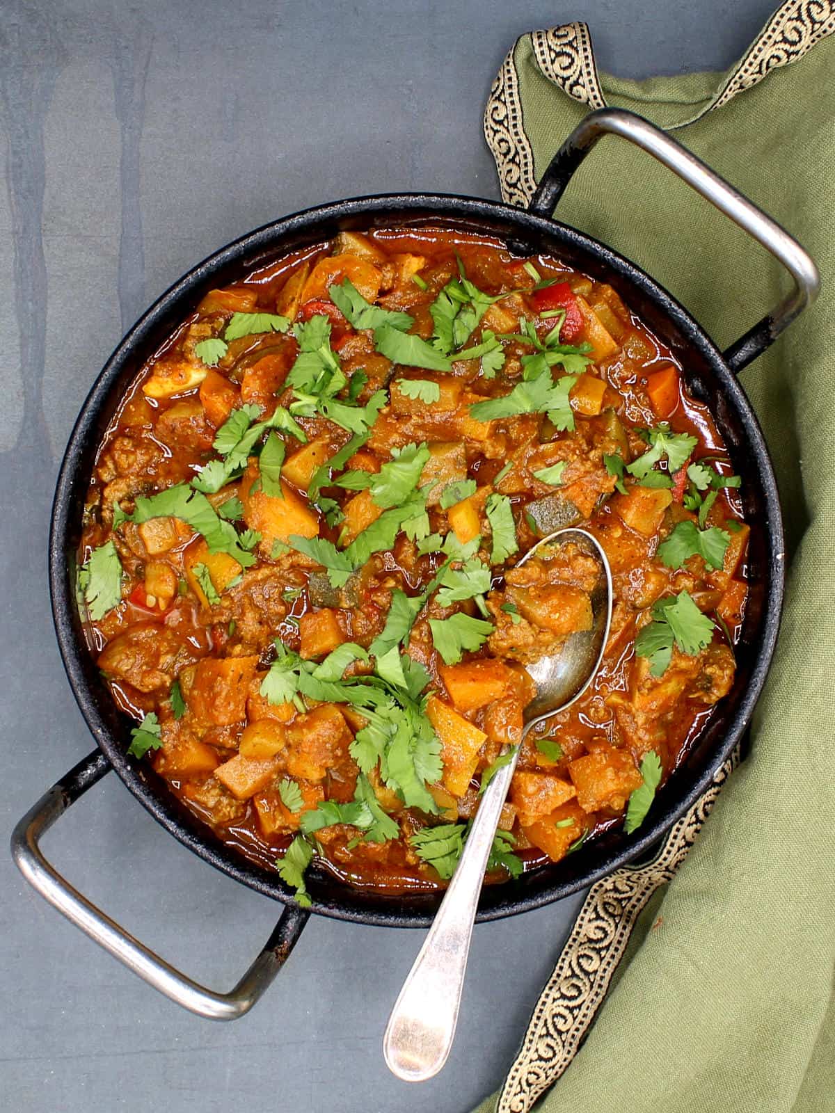 Indian curry with veggies and meat in karahi with spoon.