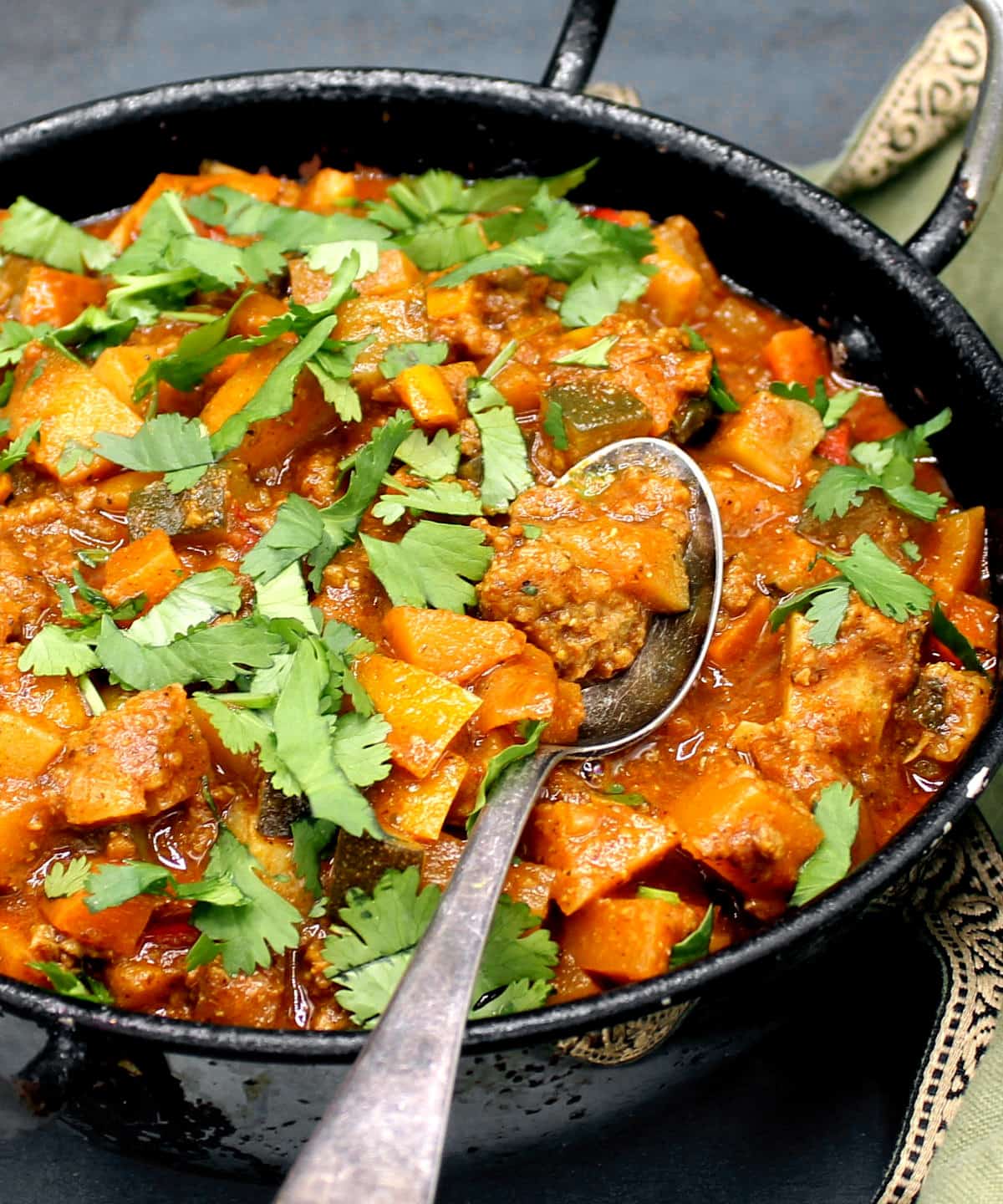 Curry with mince and veggies in karahi with a spoon.