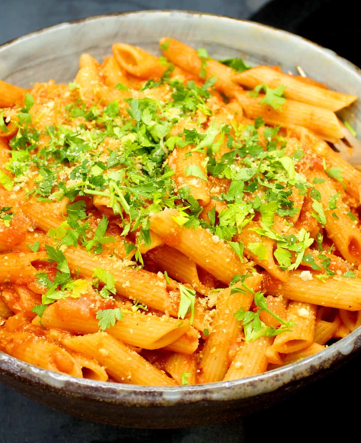 Vegan Pasta Amatriciana in a big bowl with penne pasta, tomato sauce, parsley and cashew parmesan.