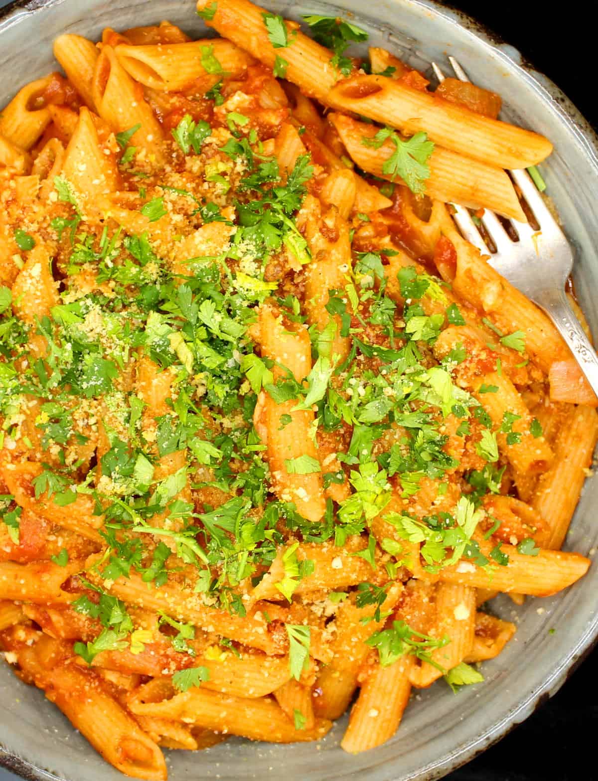 Closeup of Vegan Pasta Amatriciana in a big bowl with penne pasta, tomato sauce, parsley and cashew parmesan.