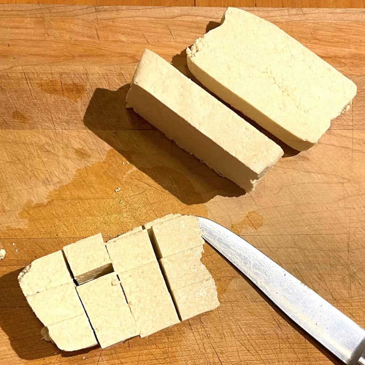Tofu slices on wooden chopping board with knife.