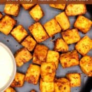 Crispy air fryer tofu cubes on a black plate with dipping sauce.