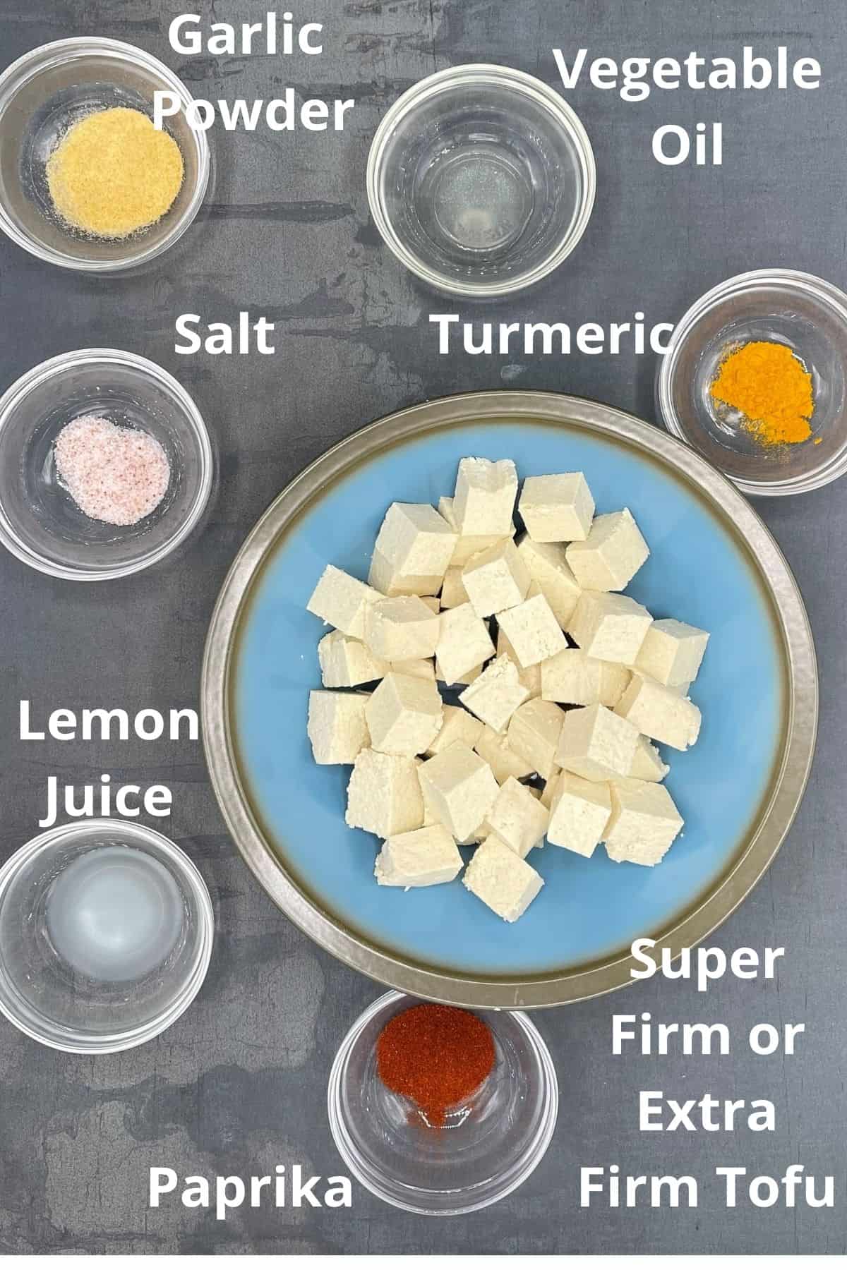 Photo of ingredients for air fryer tofu, with an overlay of the names, including garlic powder, vegetable oil, salt, turmeric, lemon juice, paprika and tofu.