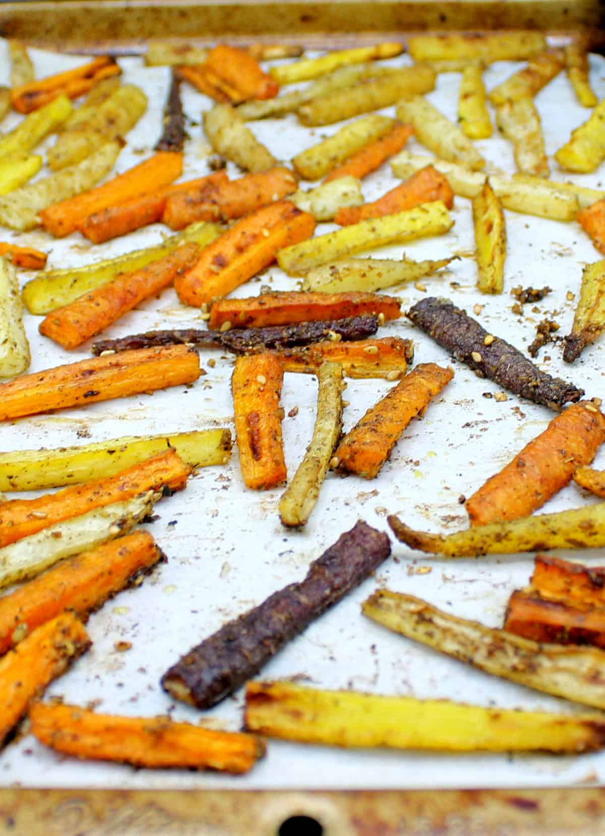 Roasted carrots with zaatar and olive oil on parchment paper in a baking sheet, arranged in a single layer.