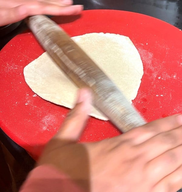 Sourdough roti being rolled on red surface.