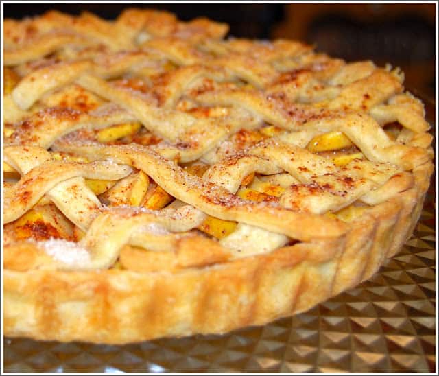 Photo of a vegan apple tart with lattice top and flaky crust on a glass dish.