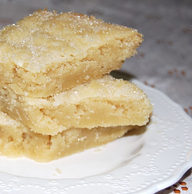 Photo of three vegan coconut shortbread cookies stacked on a decorative white plate.