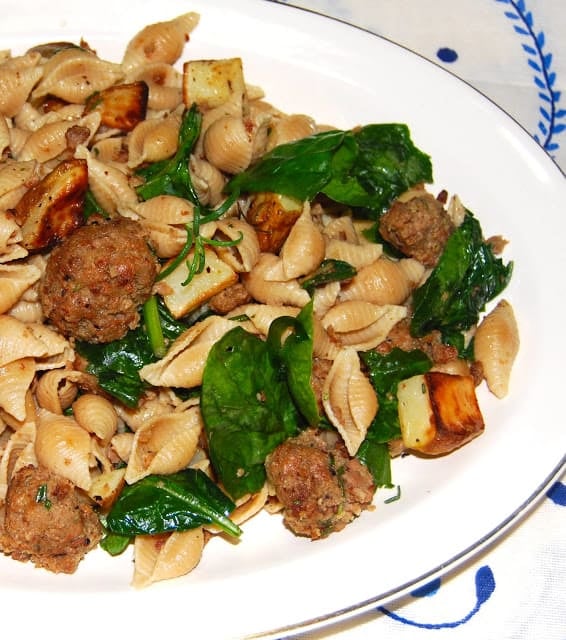 Shell pasta with vegan meatballs, spinach and potatoes in white platter.