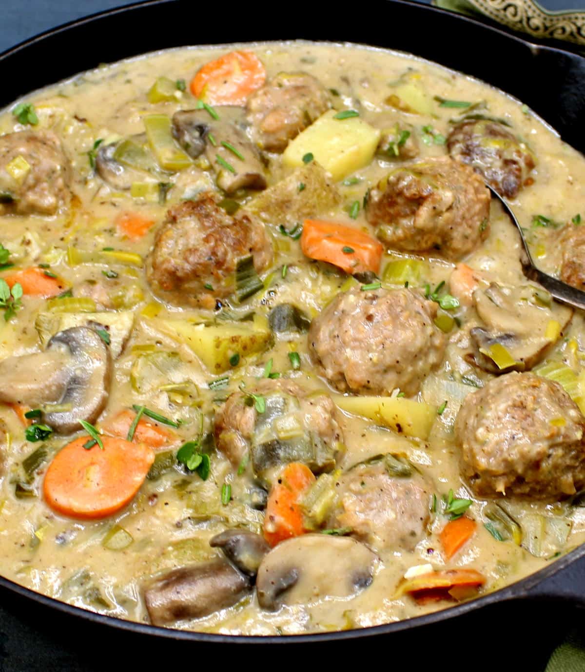 Photo of a creamy, thick vegan meatball fricassee with herbs, meatballs, carrots, potatoes, mushrooms and cajun spices.