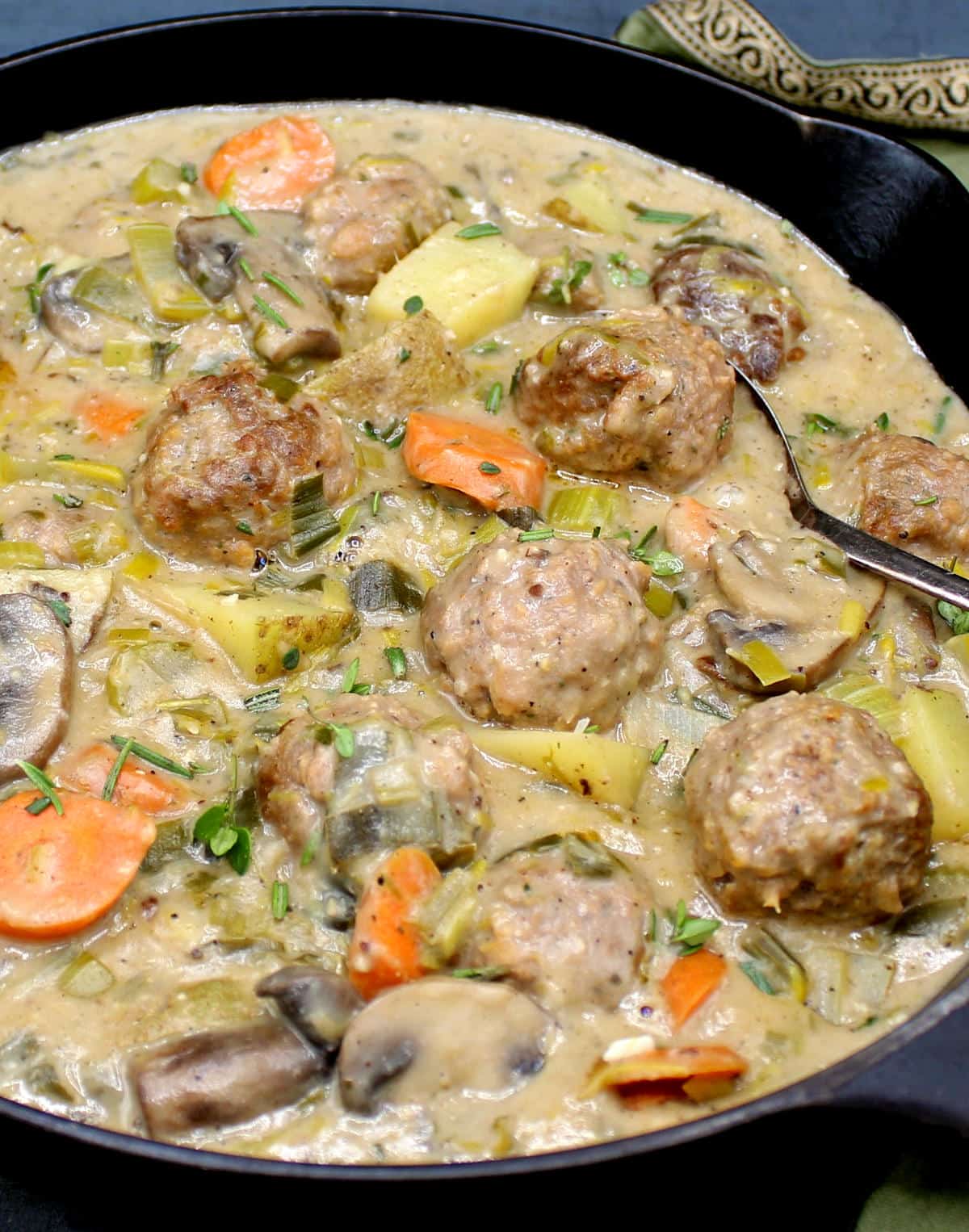 Photo of a creamy, thick vegan meatball fricassee with herbs, meatballs, carrots, potatoes, mushrooms and cajun spices.