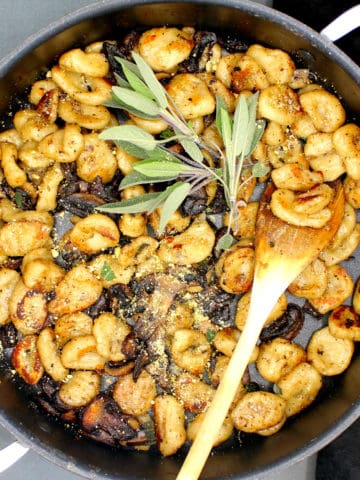 Vegan sage butter gnocchi in a pan with ladle and a sprig of sage.