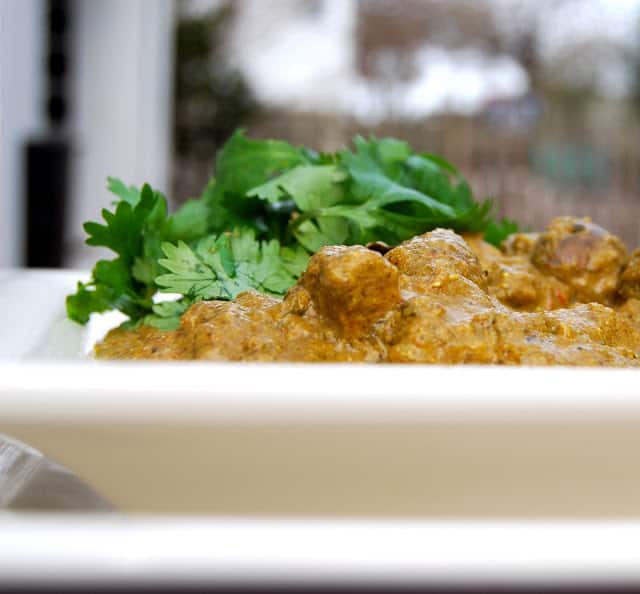 Photo of vegan spinach "chicken" curry in a  white plate with cilantro.