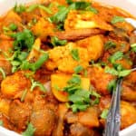 A photo of vegetable vindaloo with potatoes, cauliflower and mushrooms in a white bowl with a spoon