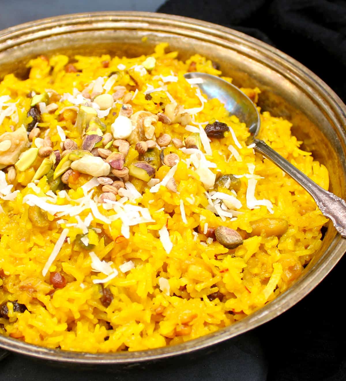 Photo of zarda pulao in a silver serving dish with nuts and dry fruits and shredded coconut.