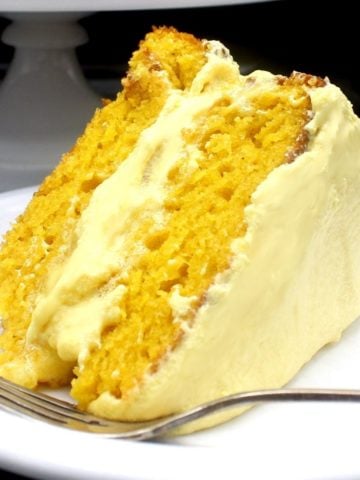 Mango cake slice with mango frosting on white plate with fork.