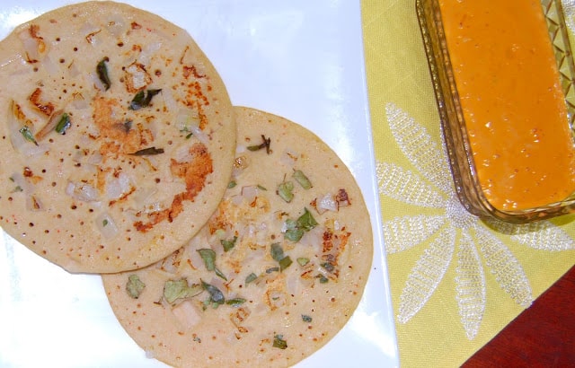 Two brown rice uthappams in white plate on yellow napkin.
