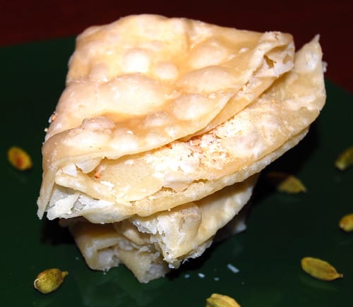 Photo of a stack of chavde or mande on a green plate with cardamom pods scattered around.