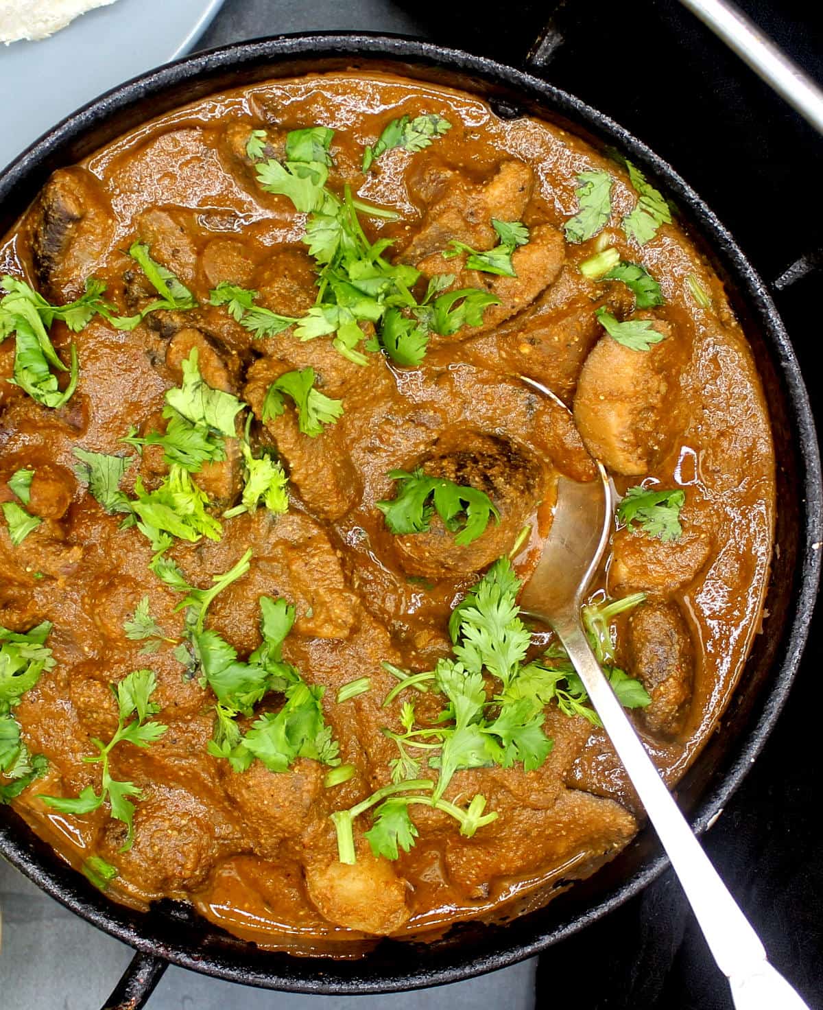 Overhead closeup photo of my dad's not-mutton mushroom curry in a karahi with cilantro garnish and a spoon.
