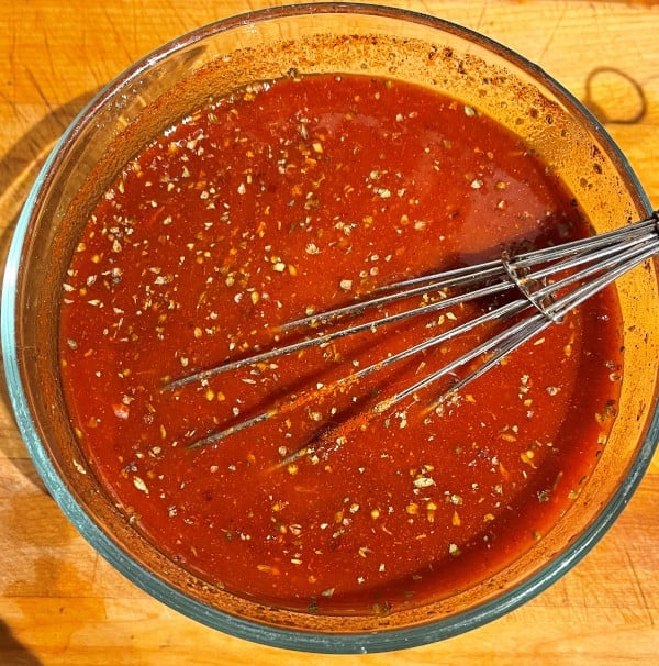 Spices and herbs whisked with enchilada sauce in bowl.