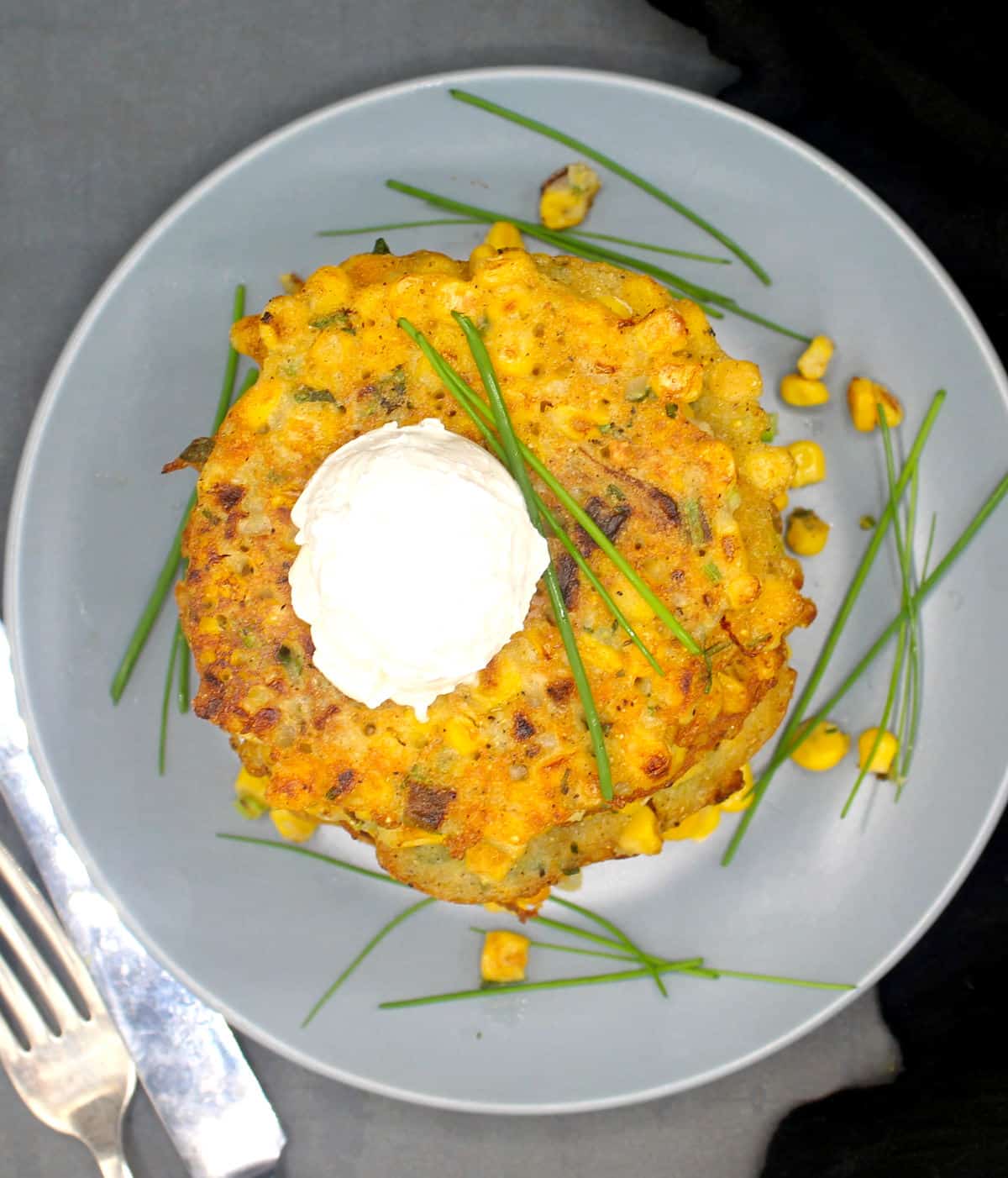 Overhead shot of vegan corn fritters on gray plate with chives and cream cheese.