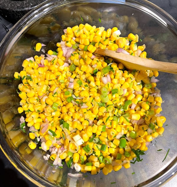 Bowl filled with corn, onions, herbs and other ingredients.