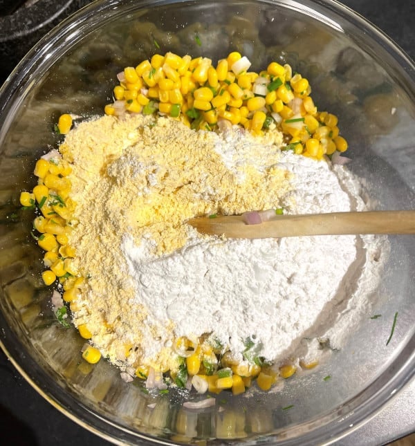 Cornmeal and flour added to bowl with corn kernels.