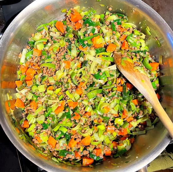Carrots added to leeks in pan with ladle.
