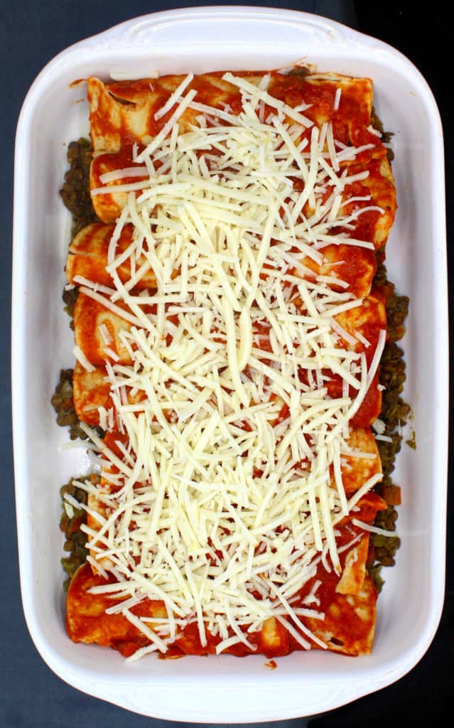 Enchiladas assembled in white baking dish with vegan cheese sprinkled on top.