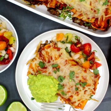 Vegan enchiladas served with a fresh tomato salsa, guacamole on a white plate with a fork.