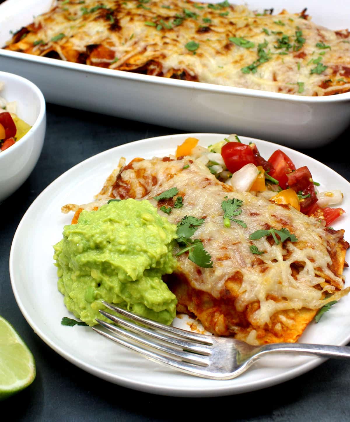 Vegan enchiladas served with a fresh tomato salsa, guacamole on a white plate with a fork.