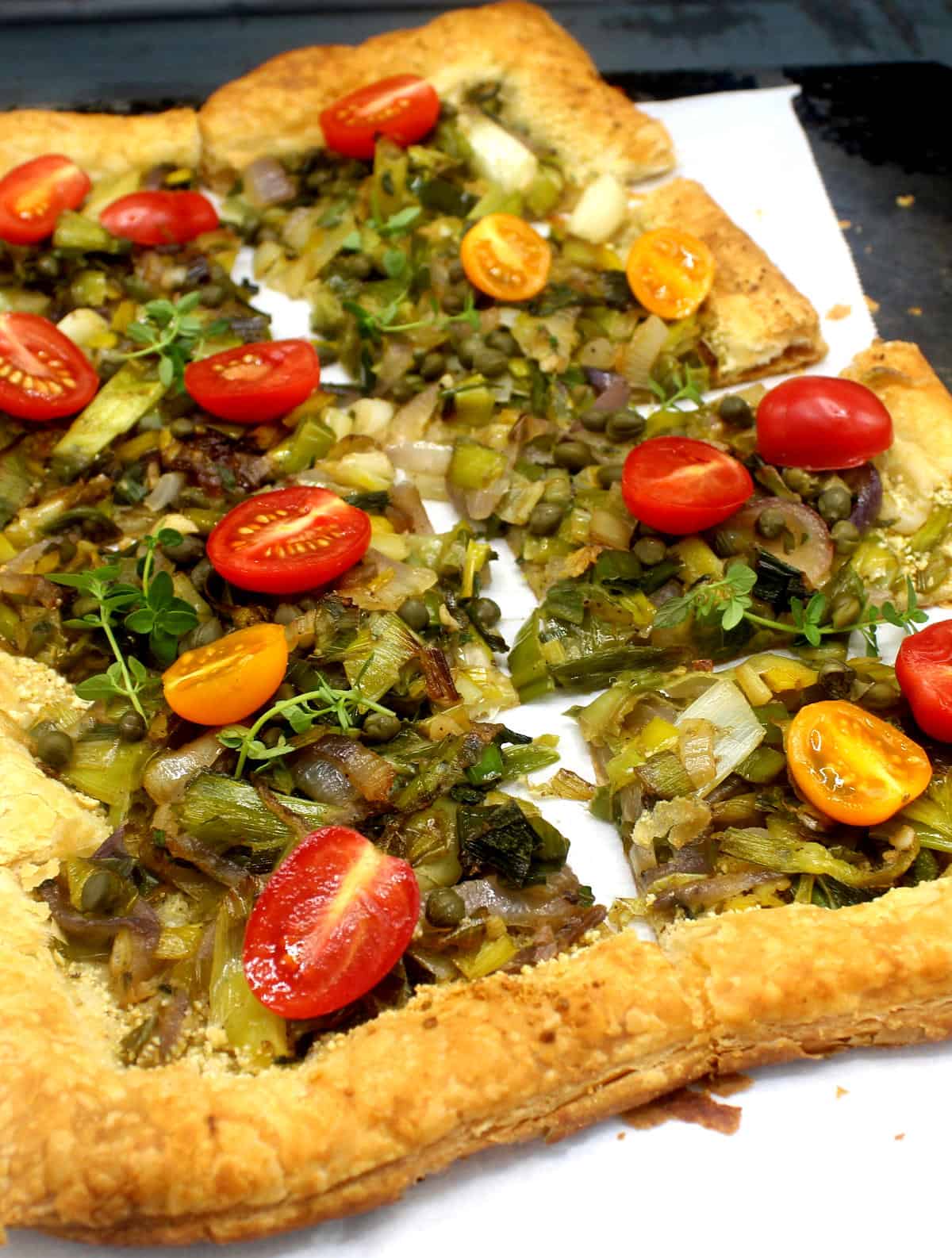 Photo of vegan leek and scallion pizza with crispy puff pastry crust and topped with scallions, leeks, cherry tomatoes and capers.