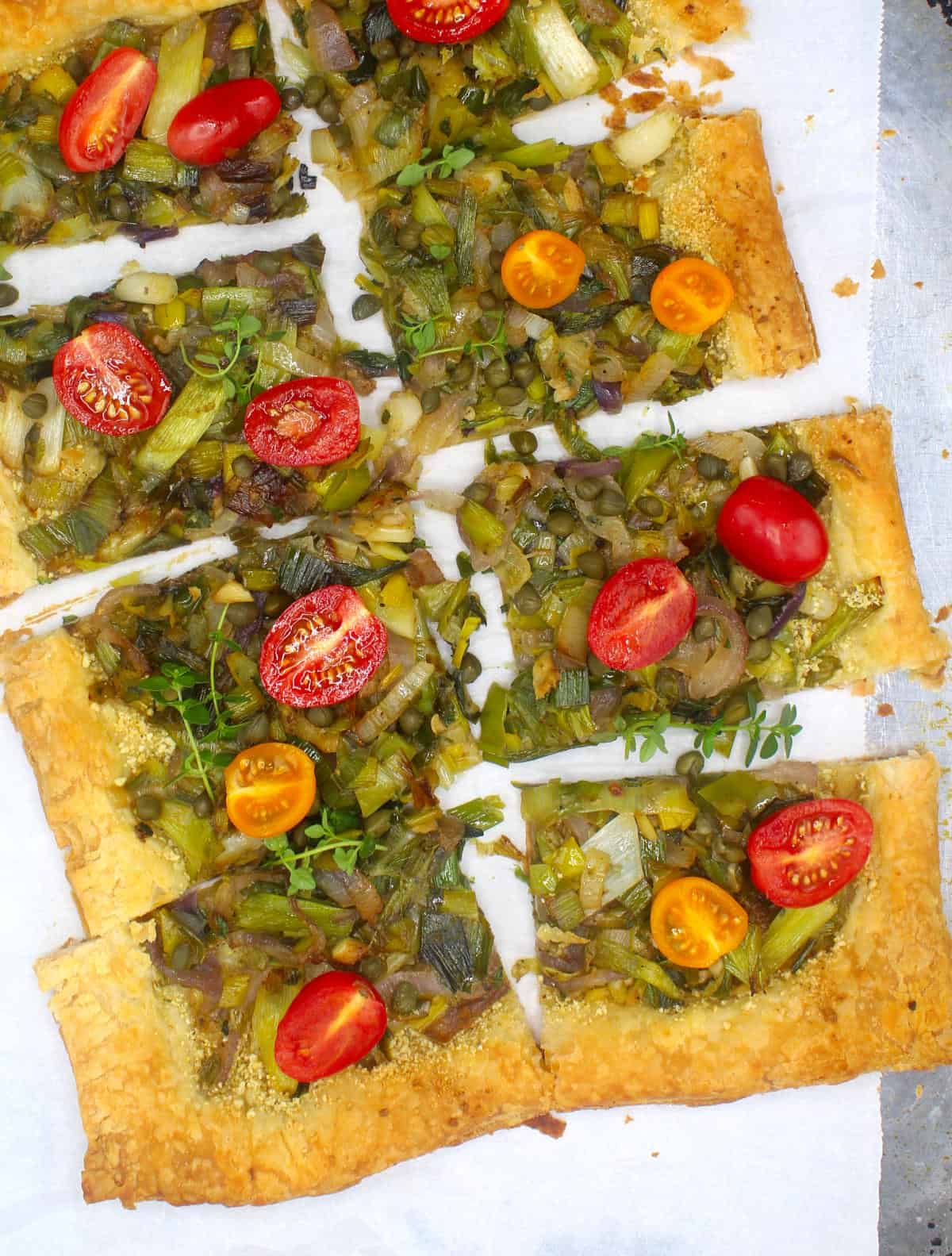 Overhead photo of a vegan leek and scallion puff pastry pizza with cherry tomatoes and fresh sprigs of thyme.