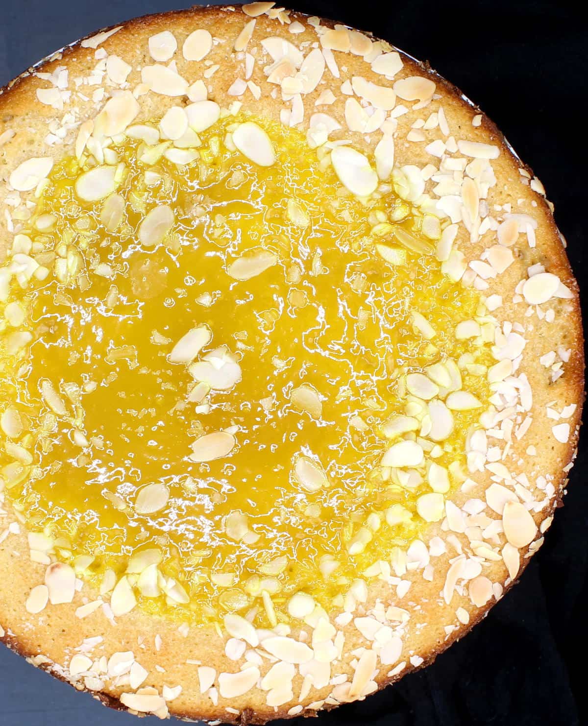 An overhead photo of the vegan lemon cake with lemon curd topping and sliced almonds.