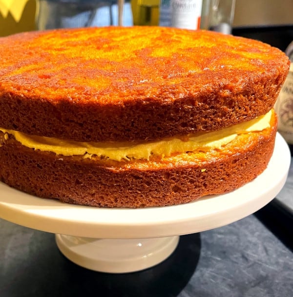 Mango cake being iced on cake stand.