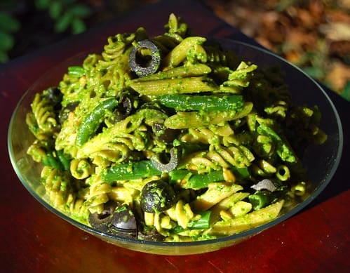Pasta with vegan spinach pesto, green beans and olives in a glass bowl.