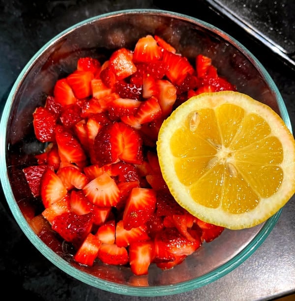 A bowl of sliced strawberries with half a lemon.