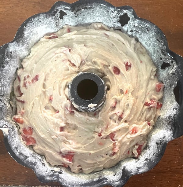 Cake batter with strawberries scraped into bundt cake pan.