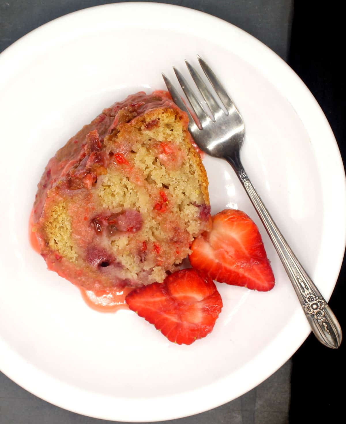 Overhead shot of a slice of vegan strawberry cake on a white plate with fresh strawberries and a fork.