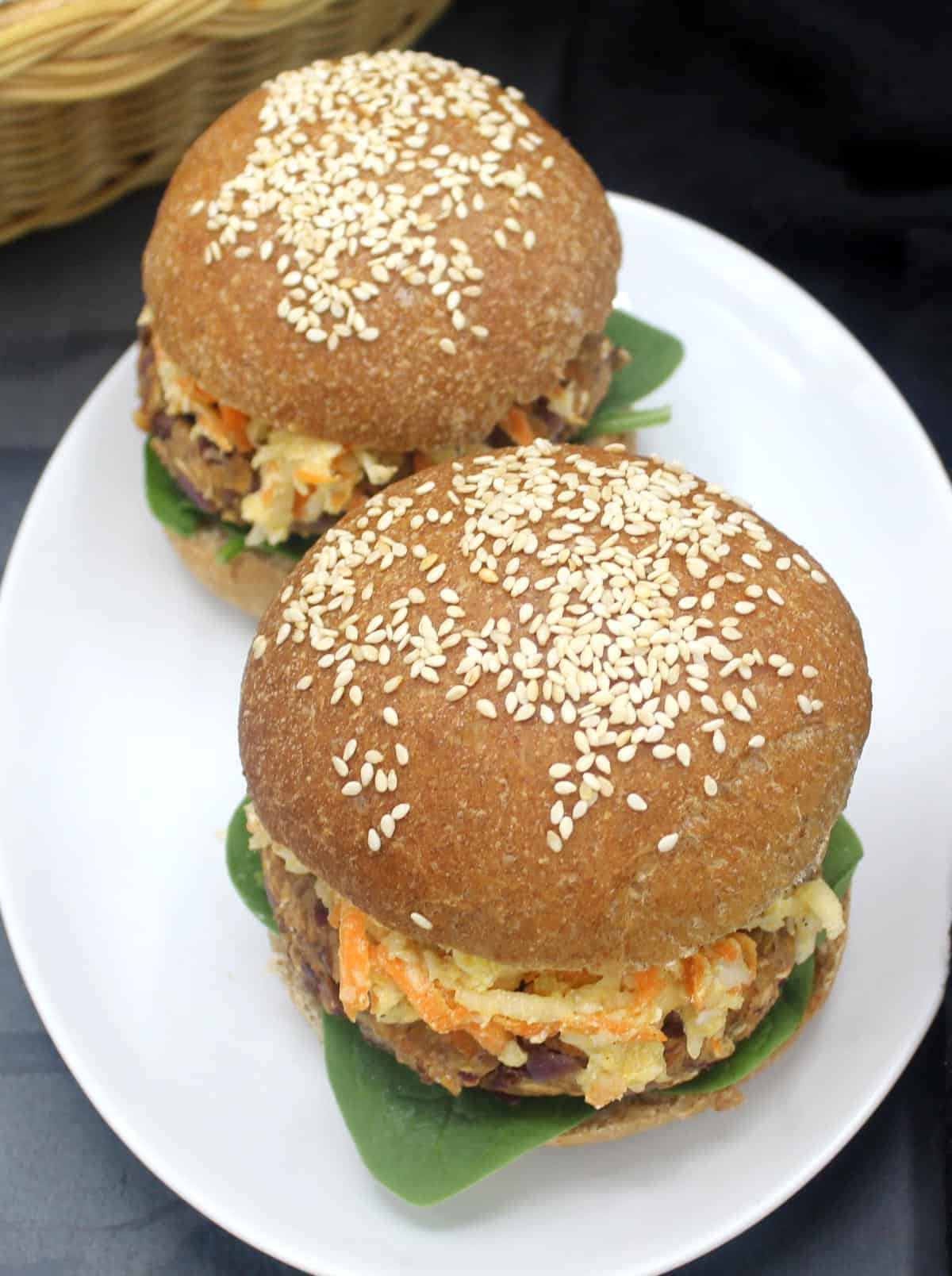 Photo of two vegan veggie burgers made with whole wheat burger buns on a white plate.