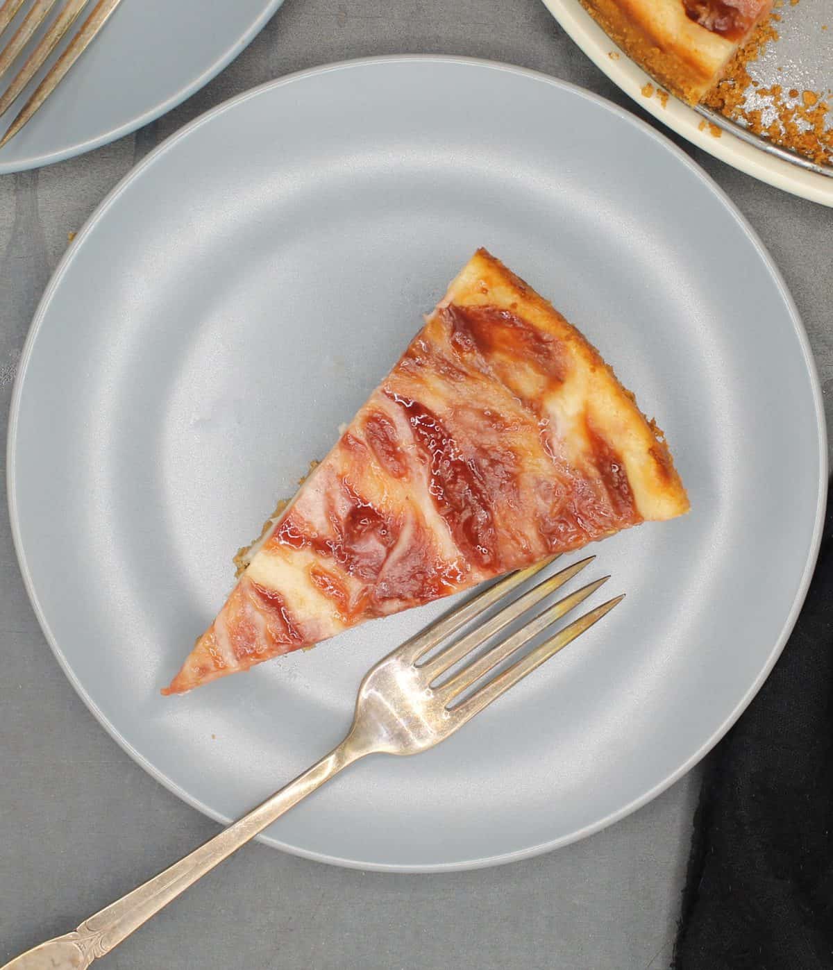 Photo of a single slice of vegan strawberry rhubarb cheesecake on a gray plate with a fork.