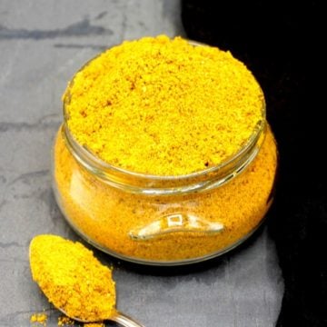 Photo of curry powder in a glass jar with a spoon next to it.