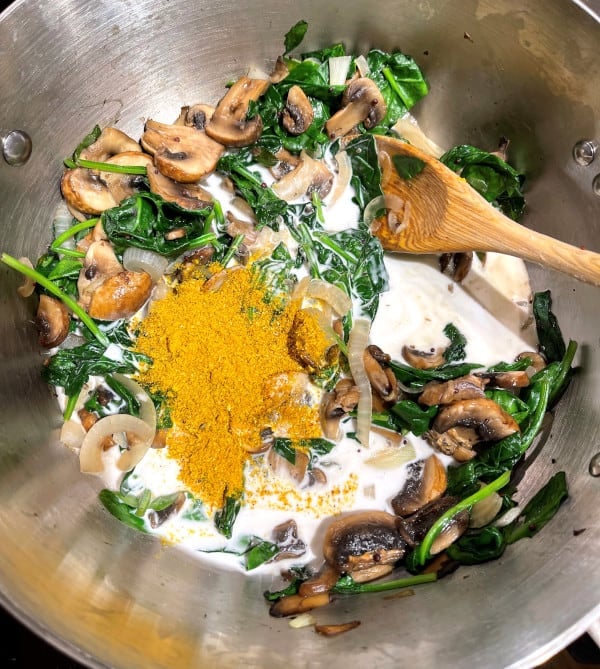 Curry powder added to mushrooms and spinach with coconut milk in skillet.