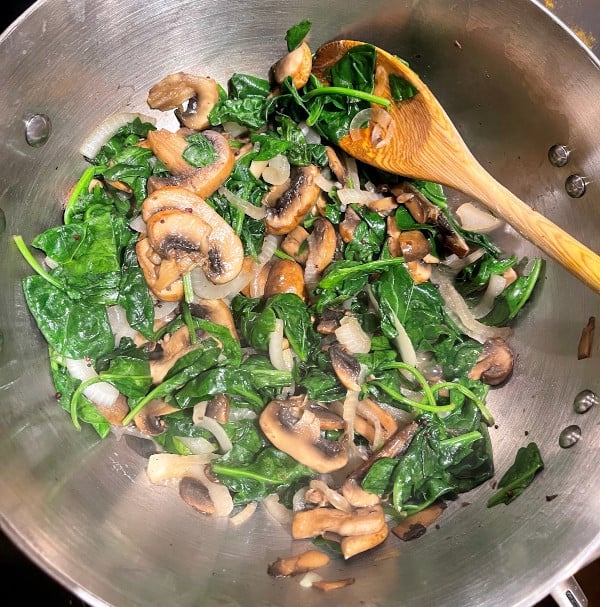 Spinach and mushrooms in skillet with wooden ladle.