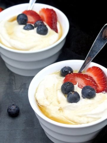Vegan yogurt in white bowls topped with slices of strawberries and blueberries.