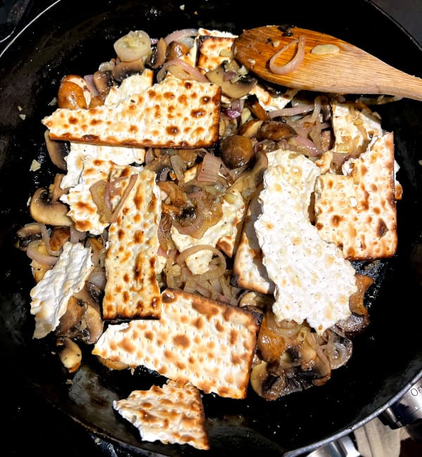 Shards of matzo crackers added to onions and mushrooms in cast iron skillet.