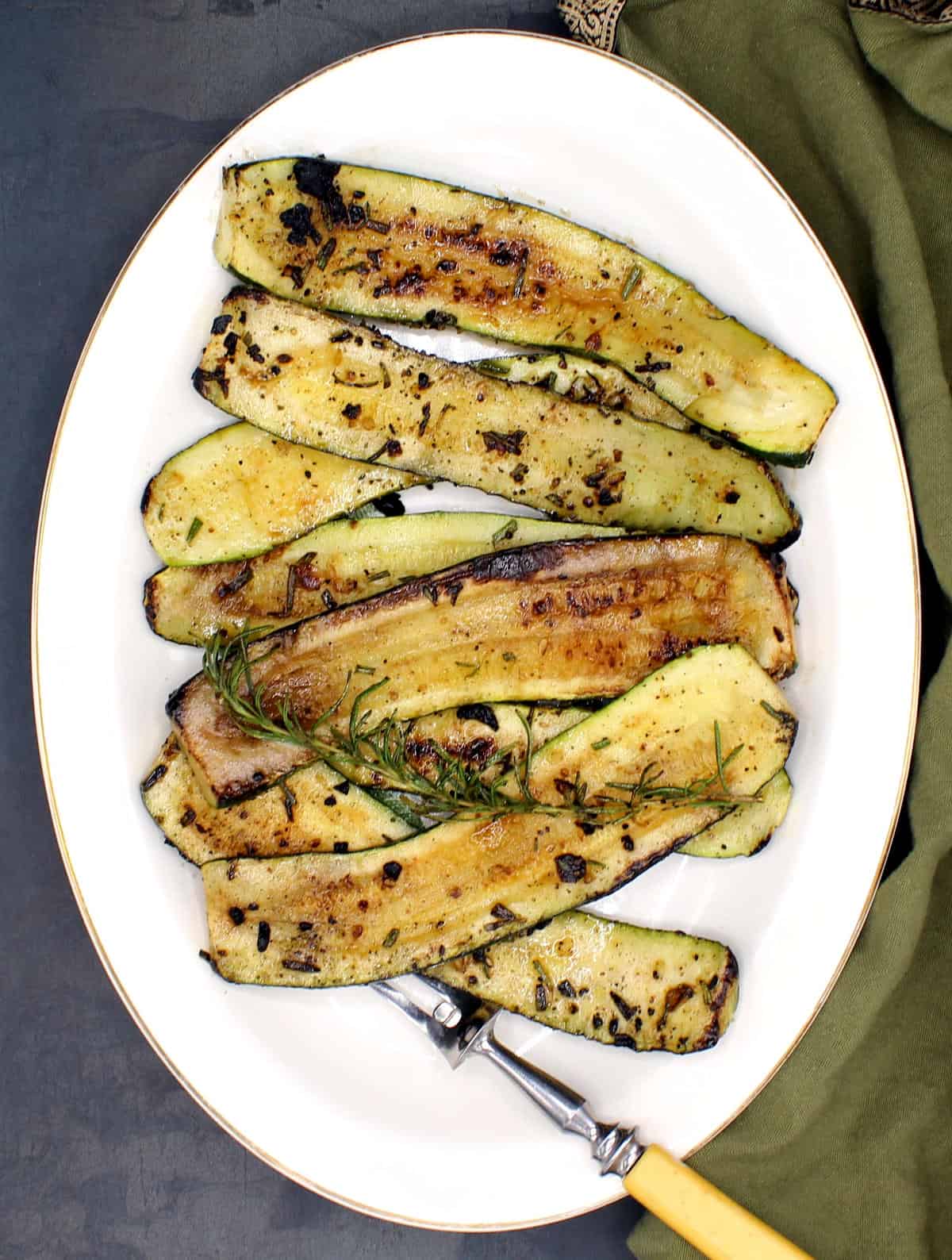 Slices of pan-roasted zucchini arranged in a platter with a steak serving fork,